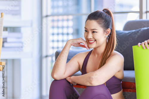 Two Millennial Asian young healthy slim strong sexy female sporty models in casual crop top sportswear sitting on floor smiling holding folding yoga mat together in living room with guitar on sofa Free Download Two Millennial Asian young healthy slim strong sexy female sporty models in casual crop top sportswear sitting on floor smiling holding folding yoga mat together in living room with guitar on sofa - GFXLoad