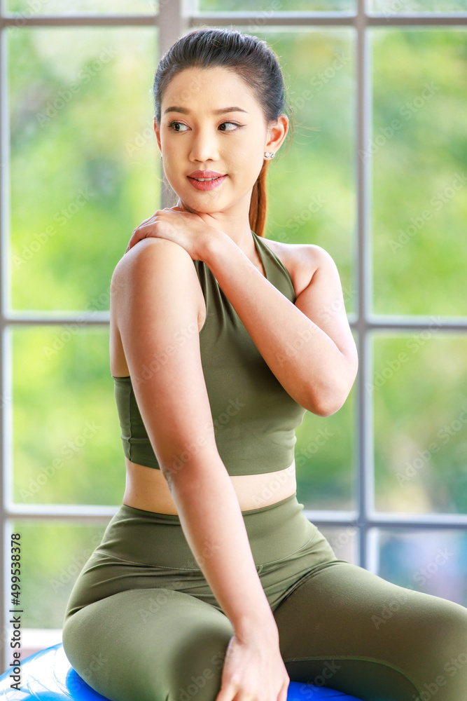 Millennial Asian young beautiful healthy slim strong sexy female sporty model in casual crop top sportswear sitting on exercise ball spreading arms stretching muscle in gym with light flare effect Millennial Asian young beautiful healthy slim strong sexy female sporty model in casual crop top sportswear sitting on exercise ball spreading arms stretching muscle in gym with light flare effect