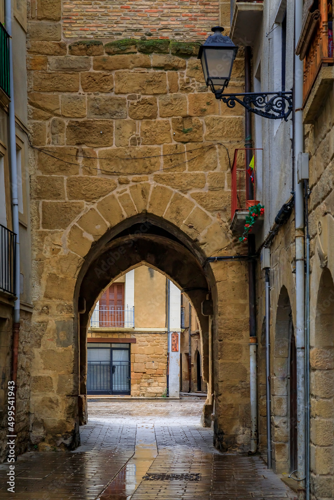Rustic medieval stone archway in a street in Olite, Spain famous for a magnificent Royal Palace castle on a rainy day with puddles on cobblestones