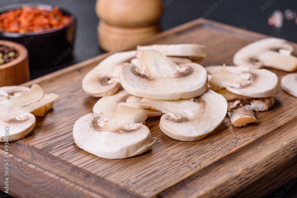 Fototapeta premium Beautiful young white champignons torn to slices on a dark concrete background