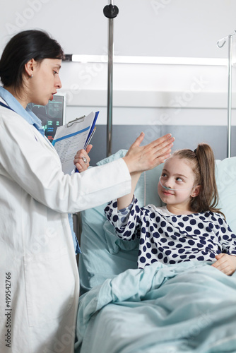Happy cheerful young patient highfive pediatric expert while in medical examination room. Healthcare facility pediatrician specialist highfive sick little girl while in patient treatment ward room.