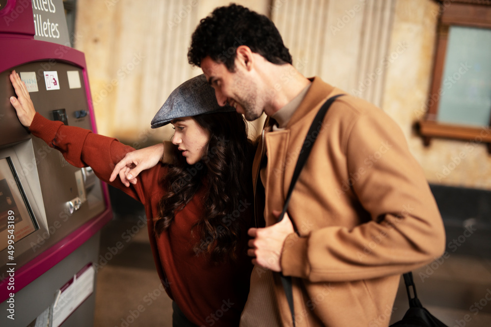 Beautiful loving couple buying train ticket at self service vending machine on the station. Happy woman and man travel together Beautiful loving couple buying train ticket at self service vending machine on the station. Happy woman and man travel together