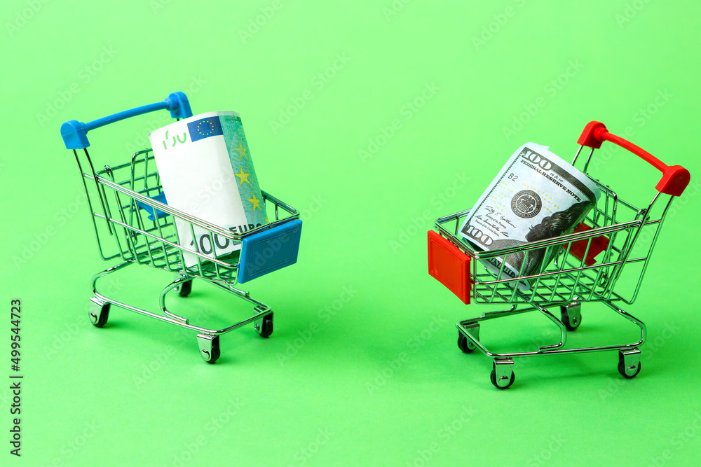 Saving and Shopping Concepts. Two Shopping Trolleys Carts With US Dollars and Euro Currency Banknotes Over Trendy Green Background.