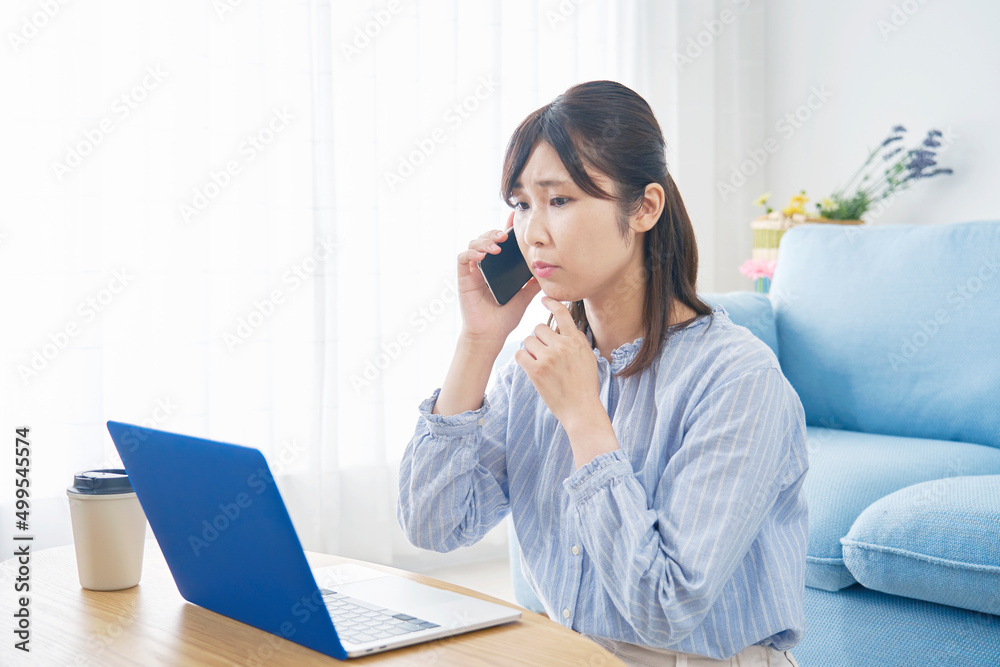 女性 ノートパソコンを見て電話する リビング 女性 ノートパソコンを見て電話する リビング