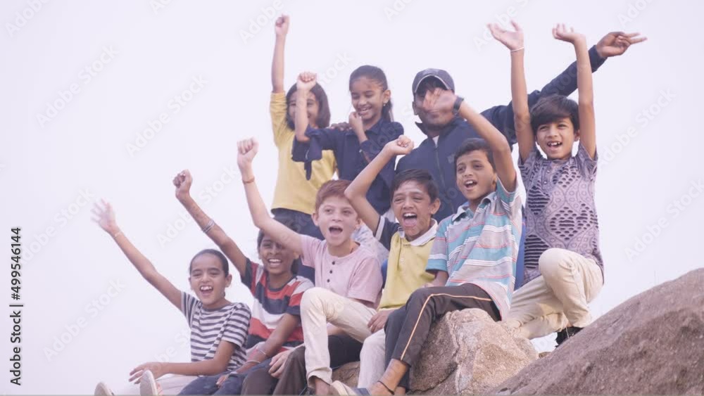 Group of hiking kids shouting with mentor after reaching destination on top of mountian during summer holidays - concept of vacation, holydays and happiness Group of hiking kids shouting with mentor after reaching destination on top of mountian during summer holidays - concept of vacation, holydays and happiness