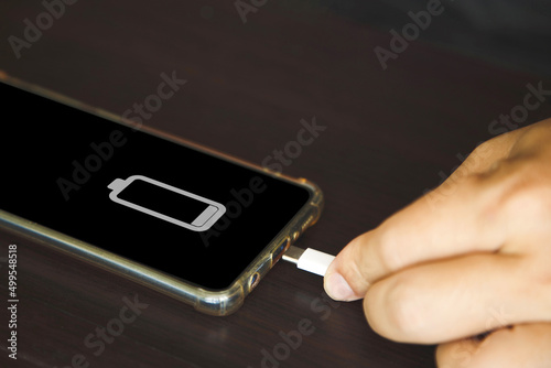 Obraz na plátně Close up a man hands using a USB tye C cable to charge mobile phone on wooden ta