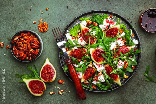 Delicious summer salad with figs, feta cheese, walnuts, arugula and sweet jam dressing on rusty green table background, top view, negative space
