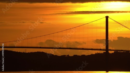 Askoy bridge during amazing golden sunset - Dark silhouette of bridge with passing traffic - Vibrant orange sky and sun above bridge tower - Bergen Norway static photo