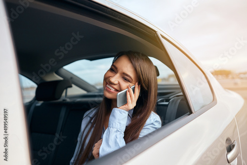 Businesswoman talking on phone while travelling in a taxi. Woman sitting on back seat of car using laptop and phone