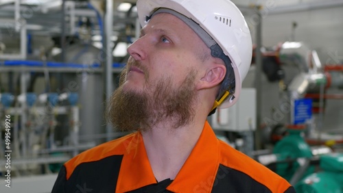 Close-up of the face of an engineer in a white helmet with a beard in the building of an industrial production workshop for pumping oil and gas condensate. Petrochemical industry