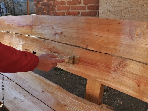 manual varnishing of the textured surface of a wooden bench in country style, a man's hand applies a layer of varnish with a brush on the surface of a handmade wooden furniture
