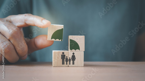 senior's hand complete umbrella over family icon on wooden cube blocks, for life or group insurance photo