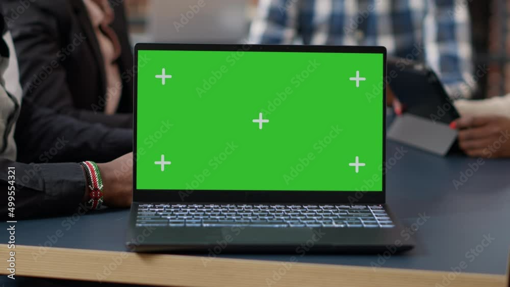 Laptop display with green screen background on office desk, people attending business meeting. Isolated mockup template with blank chroma key and copy space on computer screen. Close up.