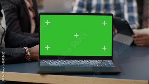 Laptop display with green screen background on office desk, people attending business meeting. Isolated mockup template with blank chroma key and copy space on computer screen. Close up. photo