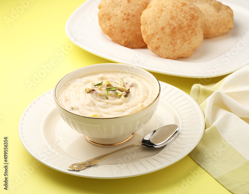 Shrikhand & Puri, Shrikhand is an Indian sweet dish made of strained curd,garnished with dry fruits and saffron. Served in a ceramic bowl & plate with Puri, Deep fried flat bread.Selective focus