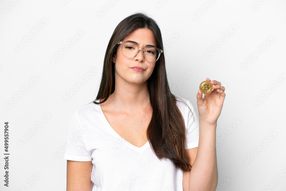 Young Brazilian woman holding a Bitcoin isolated on white background with sad expression Young Brazilian woman holding a Bitcoin isolated on white background with sad expression