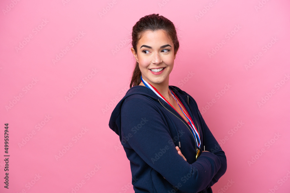 Young Brazilian sport woman with medals isolated on pink background with arms crossed and happy Young Brazilian sport woman with medals isolated on pink background with arms crossed and happy