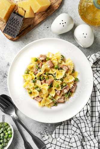 Farfalle with green peas, turkey ham and parmesan in cream sauce in a white plate on the kitchen table. Traditional Italian pasta on a light culinary background