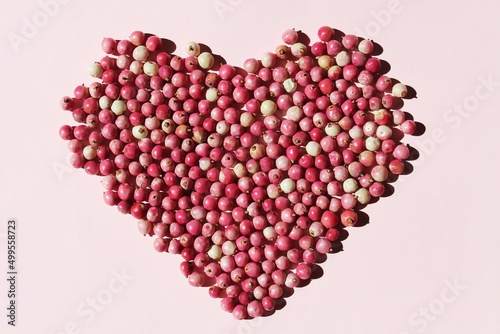 pink pepper berries in the shape of a heart, closeup in the sun , pink background 