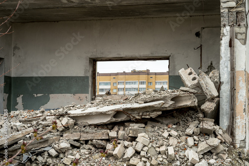 View through the destroyed window of residential buildings with a bunch of gray concrete debris in the foreground. Background