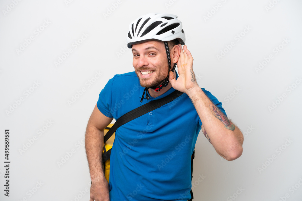 Young brazilian man with thermal backpack isolated on white background listening to something by putting hand on the ear Young brazilian man with thermal backpack isolated on white background listening to something by putting hand on the ear