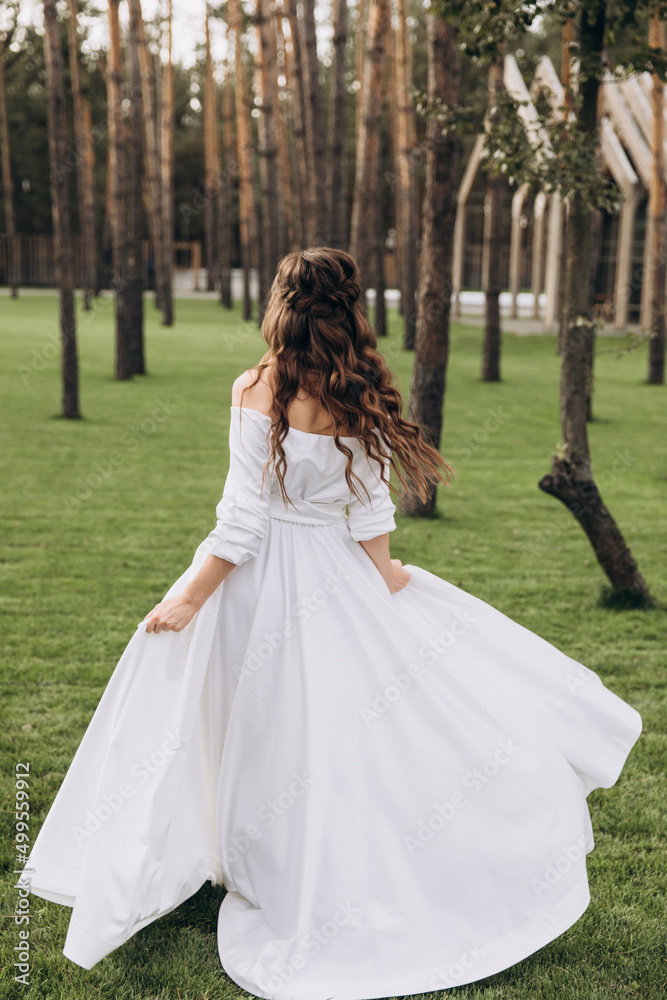 Wedding. Bride. A young girl in a white dress stands on a green glade in the forest in the summer at sunset