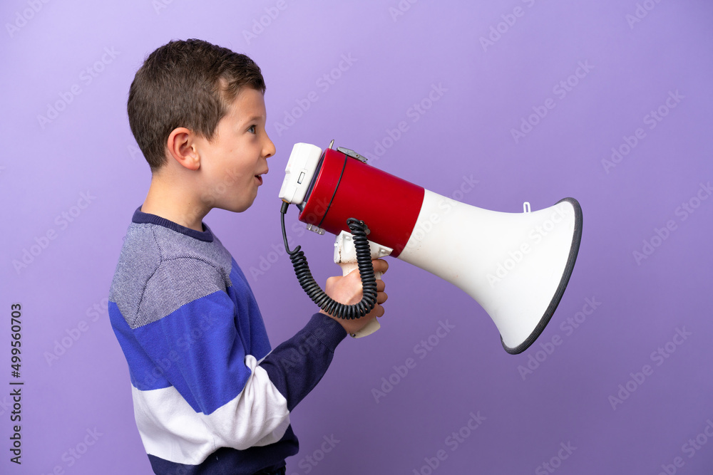 Little boy isolated on purple background shouting through a megaphone to announce something in lateral position Little boy isolated on purple background shouting through a megaphone to announce something in lateral position