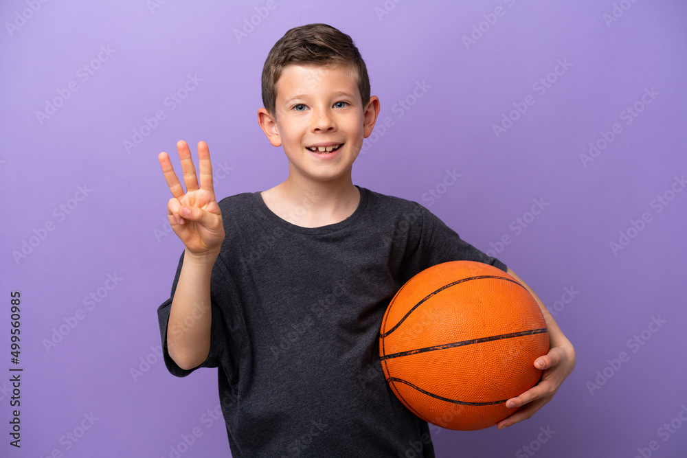Little boy playing basketball isolated on purple background happy and counting three with fingers Little boy playing basketball isolated on purple background happy and counting three with fingers