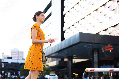 Portrait fashion woman in yellow dress walking on street of the city, smiling to side