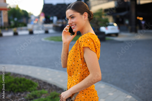 Young smiling pretty woman talking by phone, walking on the street © ty