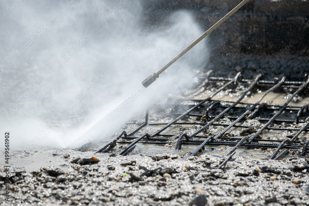 Obraz premium Worker cleaning corrosion damaged concrete bridge pillar with high pressure washer. Road bridge construction industry.