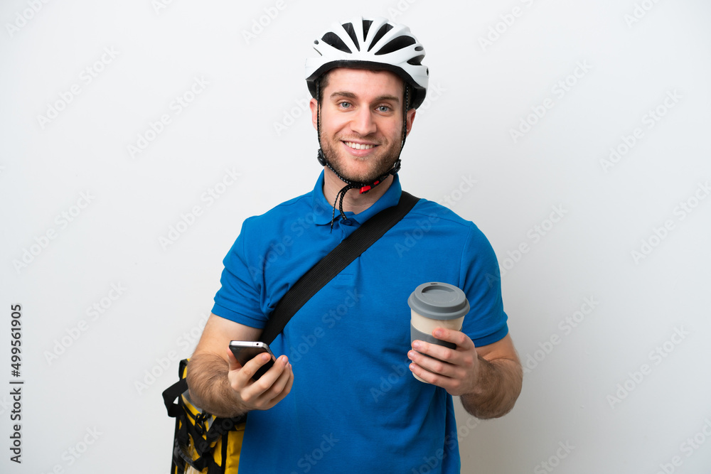 Young caucasian man with thermal backpack isolated on white background holding coffee to take away and a mobile Young caucasian man with thermal backpack isolated on white background holding coffee to take away and a mobile