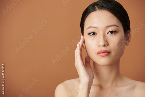Portrait of serious young woman with natual make-up touching face and looking at camera