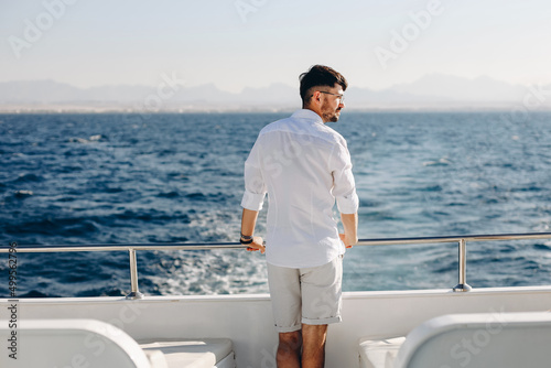 Stylish, young man in sunglasses on the deck of a cruise ship the background of the morning sunrise and the blue sky. Concept of sea travel and recreation