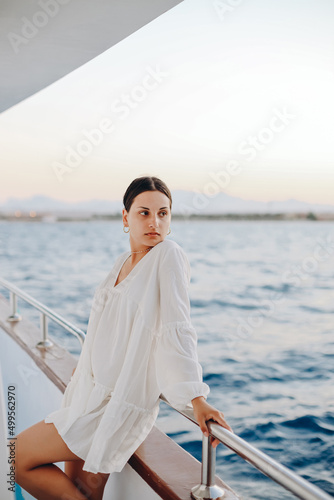 Portrait of a girl, in a white delicate dress, standing near the deck of the boat, against the background of the blue sea © Josep