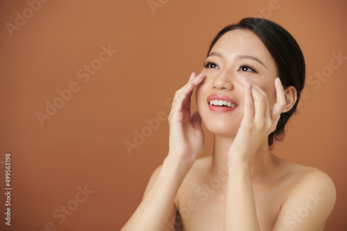 Portrait of happy young woman applying brightening and depuffing undereye moisturizer photo