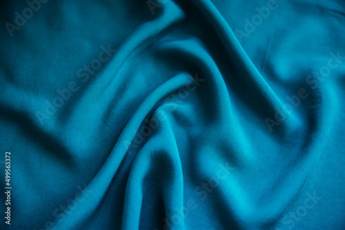 Blue wrinkled fabric lies in folds on the table with drapery.