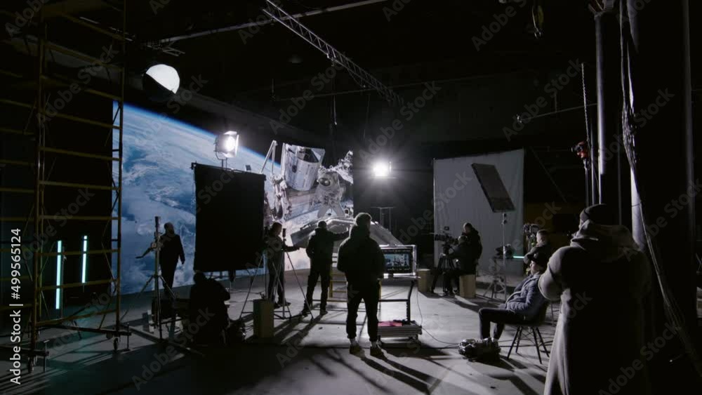 Behind the scenes of virtual production shot - Film crew working with Caucasian female astronaut stuntwoman in a spacesuit hanging on a wires against huge LED screen. Some elements furnished by NASA