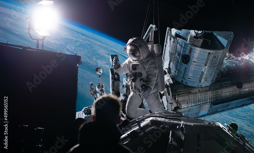 Photo Behind the scenes of virtual production shot - Film crew working with Caucasian female astronaut stuntwoman in a spacesuit hanging on a wires against huge LED screen