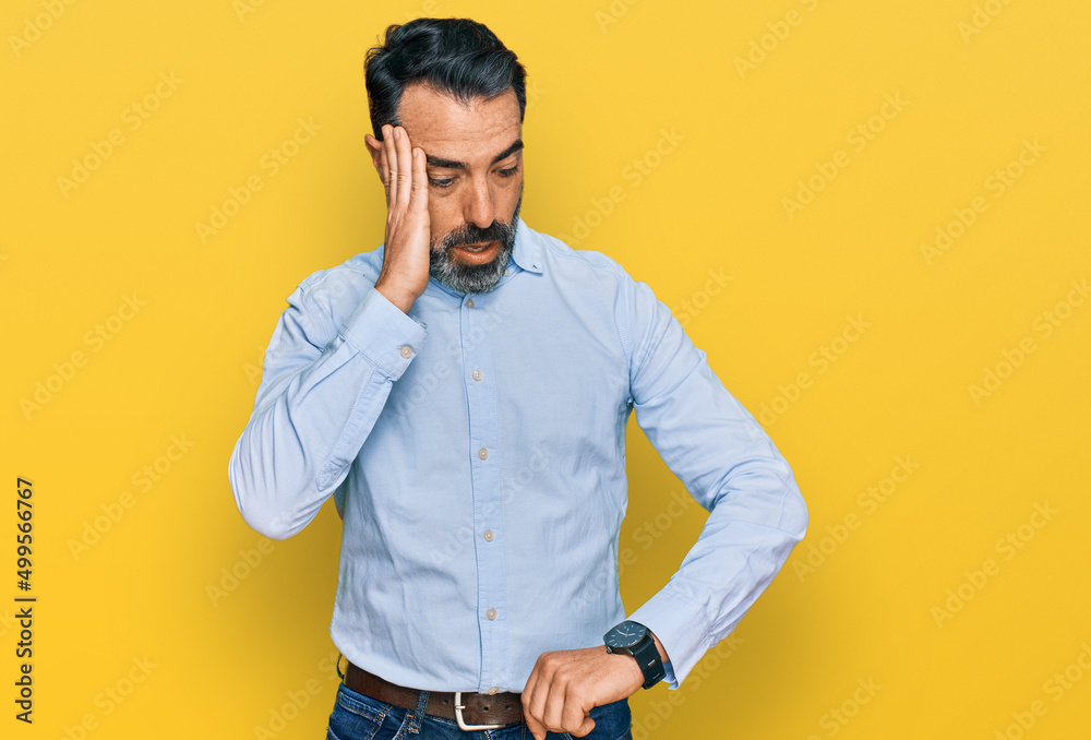 Middle aged man with beard wearing business shirt looking at the watch time worried, afraid of getting late Middle aged man with beard wearing business shirt looking at the watch time worried, afraid of getting late
