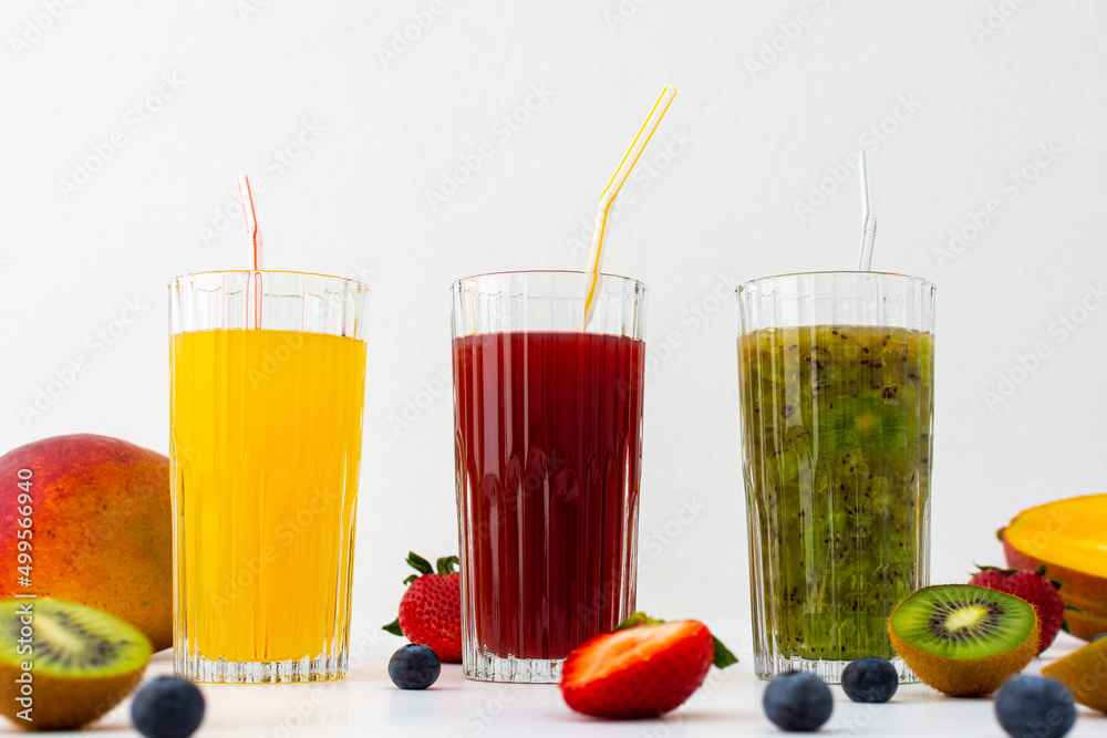 Strawberry, mango, blueberry juice and kiwi juice in glasses with a straw, fruit scattered on the table, healthy tasty sweet drinks