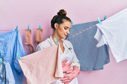 Beautiful brunette young woman washing clothes at clothesline with hand on stomach because indigestion, painful illness feeling unwell. ache concept.