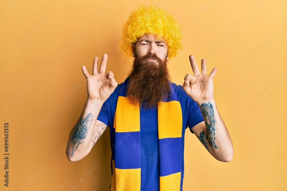 Redhead man with long beard football hooligan cheering game wearing funny wig relax and smiling with eyes closed doing meditation gesture with fingers. yoga concept.