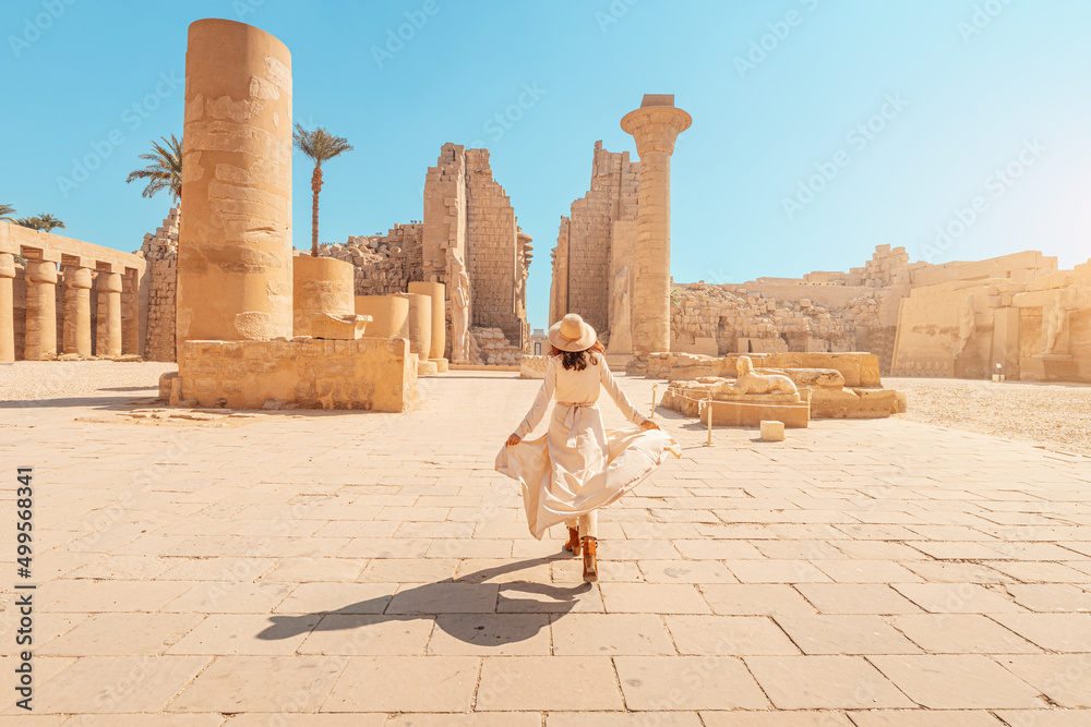 Happy woman traveler explores the ruins of the ancient Karnak temple in the heritage city of Luxor in Egypt. Giant row of columns with carved hieroglyph