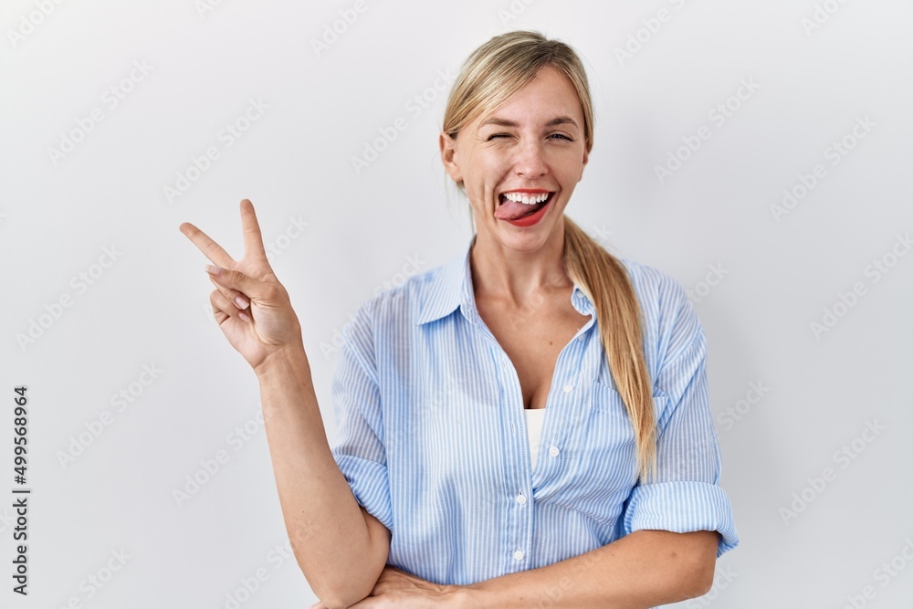 Beautiful blonde woman standing over white background smiling with happy face winking at the camera doing victory sign. number two. Beautiful blonde woman standing over white background smiling with happy face winking at the camera doing victory sign. number two.