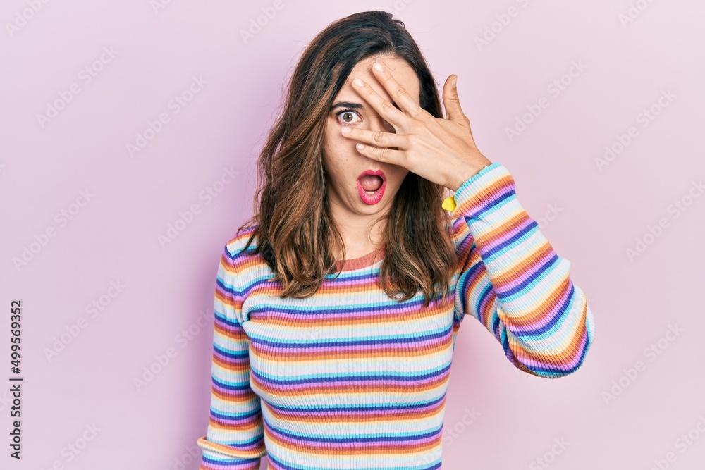 Young hispanic girl wearing casual clothes peeking in shock covering face and eyes with hand, looking through fingers with embarrassed expression.