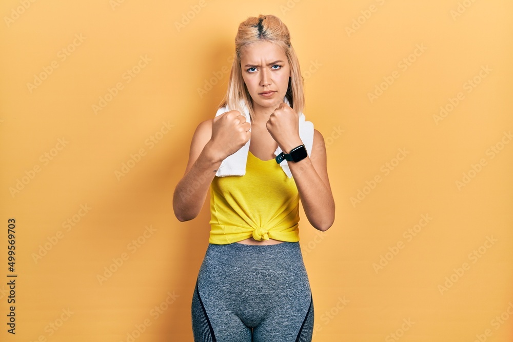 Beautiful blonde sports woman wearing workout outfit ready to fight with fist defense gesture, angry and upset face, afraid of problem Beautiful blonde sports woman wearing workout outfit ready to fight with fist defense gesture, angry and upset face, afraid of problem