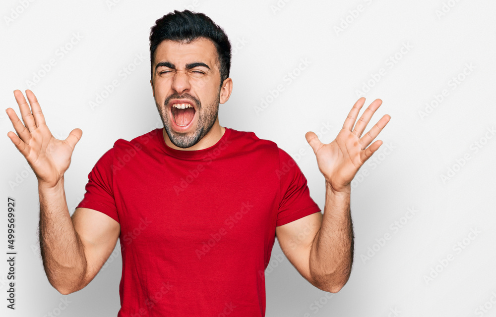 Hispanic man with beard wearing casual red t shirt celebrating mad and crazy for success with arms raised and closed eyes screaming excited. winner concept Hispanic man with beard wearing casual red t shirt celebrating mad and crazy for success with arms raised and closed eyes screaming excited. winner concept