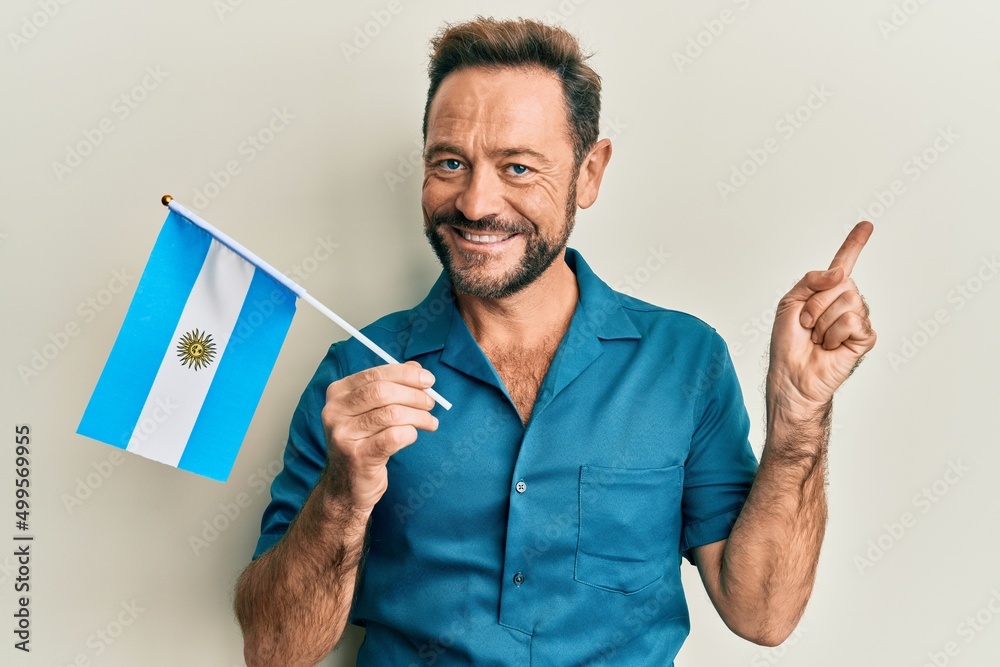 Middle age man holding argentina flag smiling happy pointing with hand and finger to the side - obrazy, fototapety, plakaty 
