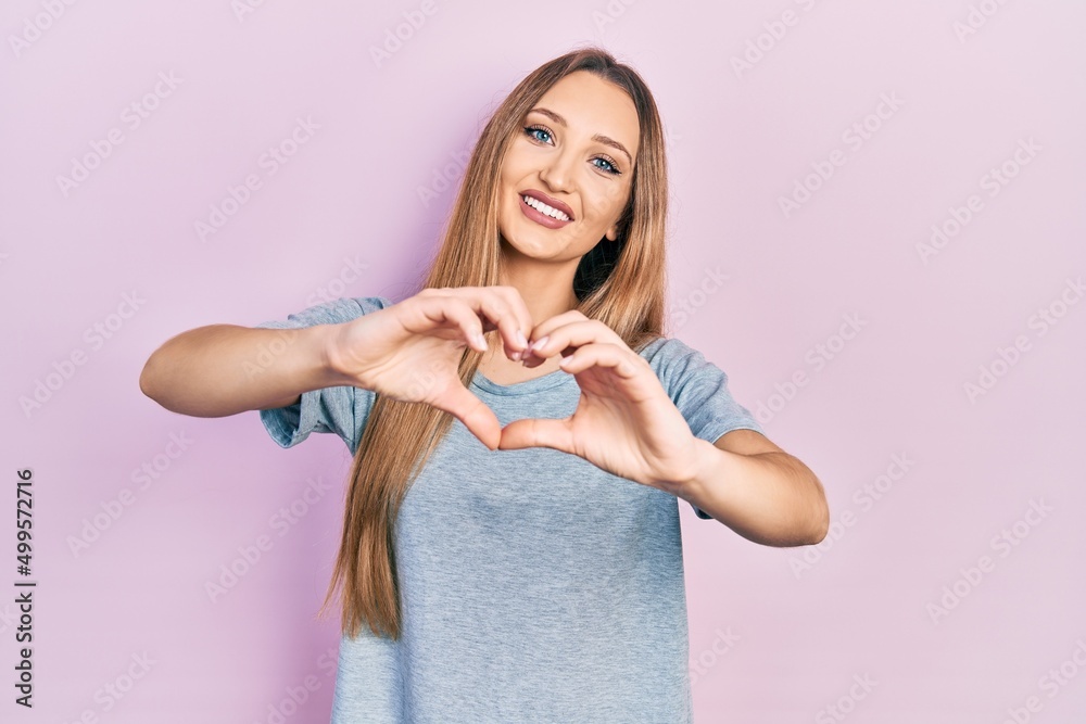 Young blonde girl wearing casual t shirt smiling in love doing heart symbol shape with hands. romantic concept. Young blonde girl wearing casual t shirt smiling in love doing heart symbol shape with hands. romantic concept.